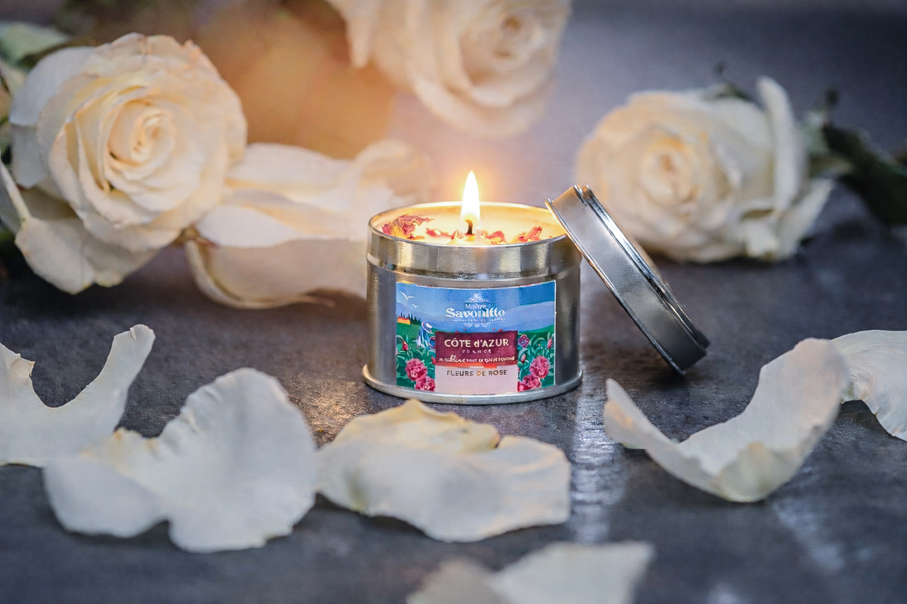 Bougie parfumée Rose – Côte d’Azur Bougie parfumée à la rose dans une boîte métal, entourée de pétales de rose blanche, ambiance élégante